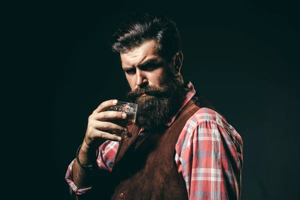 Сомельє. Гіпстер з бородою і вусами в костюмі п'є алкоголь після робочого дня. Впевнений бородатий чоловік в чорному костюмі зі склянкою віскі в лофт . — стокове фото