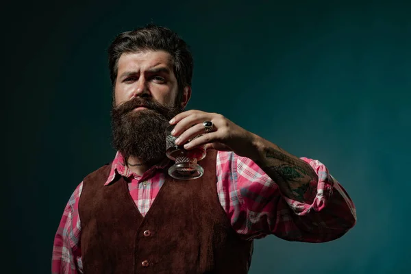 スタイリッシュでエレガントなあごひげの男バーテンダーは、ウイスキーグラスを保持しています。最高級のウイスキーを飲む。古い伝統的なウイスキードリンク - 紳士飲料. — ストック写真