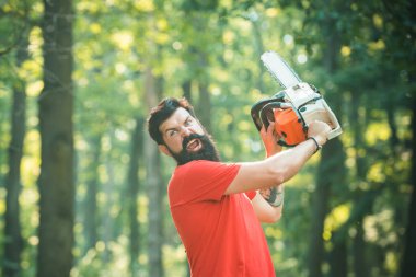 Oduncu elektrikli testereyi tutuyor. Ormansızlaşma, doğal ekosistemlerin toprak bozulması ve istikrarsızlaşmasının önemli bir nedenidir. Orman yakınında balta ile Yakışıklı genç adam.