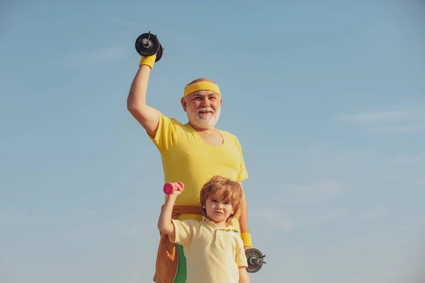 Aranyos gyerek és magas rangú ember gyakorlása a súlyzók. Nagyapja és gyermeke nem reggel gyakorolja. Apa és fia épít bicepsz és tricepsz. — Stock Fotó