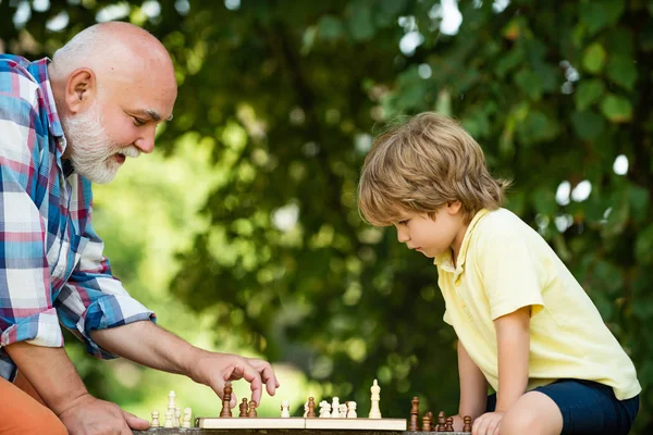 Old man with young child boy playing chess. Childhood. Grandfather and grandson concept. Chess piece. Cute boy developing chess strategy.