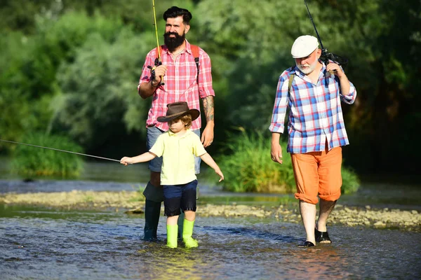 Uomo con il figlio e il padre sulla pesca fluviale con canne da pesca. Padre insegna a suo figlio la pesca contro la vista del fiume e del paesaggio. Giorno di uomini . — Foto Stock