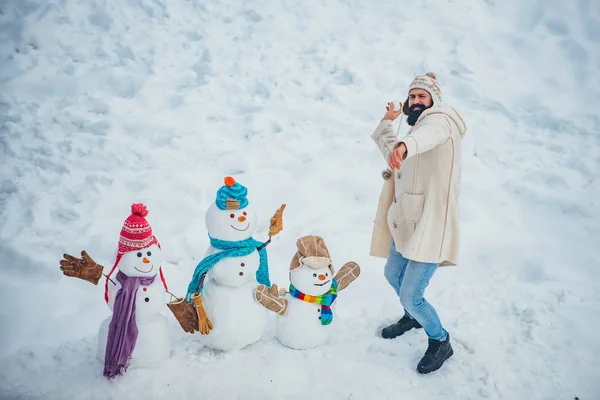 Muñeco de nieve y hombre barbudo divertido el amigo está de pie en sombrero de invierno y bufanda con nariz roja. Hacer muñeco de nieve y diversión de invierno para el hombre. Concepto de invierno . — Foto de Stock