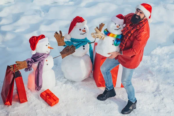 Den Winter in der Natur genießen. Wintermann. Weihnachtsmann und Schneemann auf weißem Schnee-Hintergrund. Schneemann und lustiger bärtiger Mann, der Freund steht in Wintermütze und Schal mit roter Nase. — Stockfoto