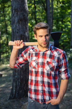 Oduncu gibi poz veren şık genç adam. Oduncu ormanda çalışıyor. Baltalı yakışıklı bir adam. Ekose gömlek bir balta ile Güçlü adam oduncu.