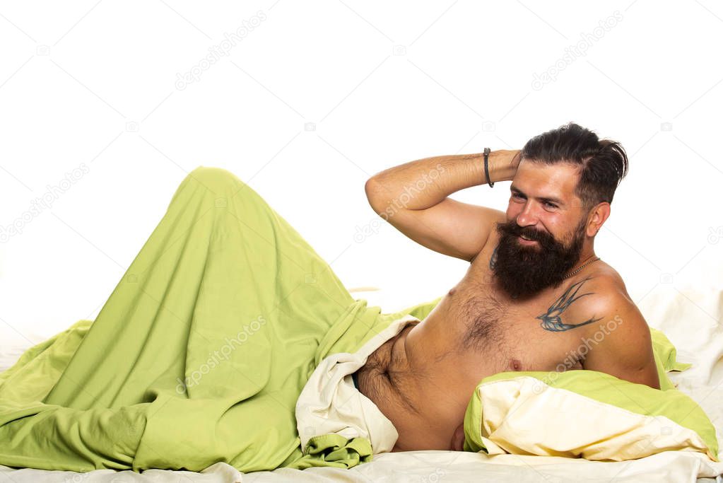 Young man is lying on bed and enjoying the morning. Attractive bearded guy holding in hands pillow in bed. Boy sleeping and dreaming.