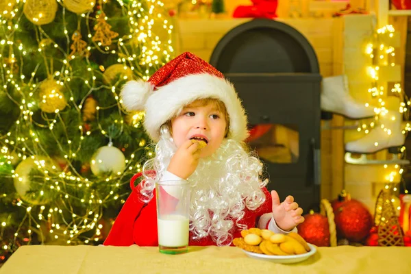 stock image Santa boy child eating cookies and drinking milk. Santa Claus - bearded funny child. Santa in home. Santa Claus takes a cookie on Christmas Eve as a thank you gift for leaving presents.