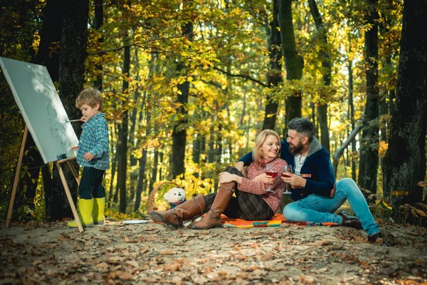 Höst familj utomhus. Ung familj njuter på en picknick. Little Happy son ritning i parken. Lära barnen att tänka på gott uppförande. Passion för konst. Vackra höst parken. — Stockfoto