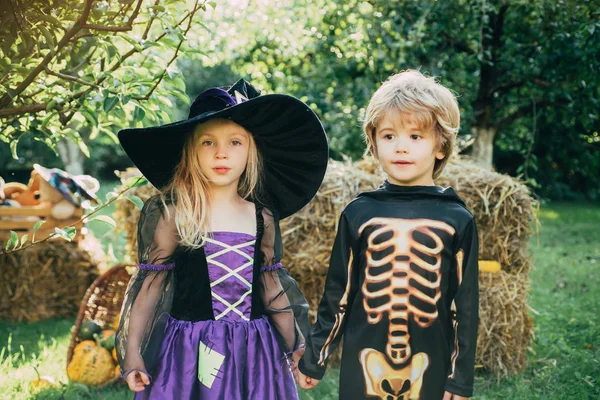 Halloween Kids Party in de tuin met pompoenen. Jack-o-lantern. Happy Halloween kinderen meisje en jongen zitten op hooi of stro op weide in de herfst. Happy Halloween met snoep kaarsen. — Stockfoto
