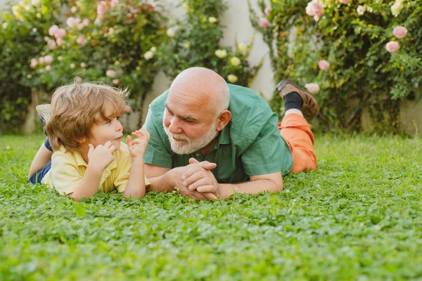 Grandson embrace his grandfather. Happy grandfather and child grandson laugh and have fun together in summer in nature. Happy father and son on meadow in summer. — Stock Photo, Image