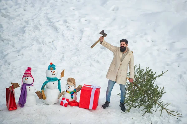 Coupe-bois avec hache dans la forêt d'hiver. Un beau bois avec une barbe porte un sapin de Noël. Jeune homme bûcheron coupe arbre de Noël dans le bois . — Photo