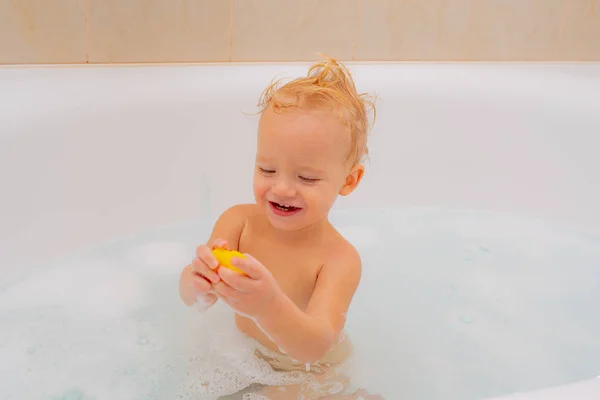 Lächelndes Kind im Badezimmer. Lustiges Baby, das in einer großen Küchenspüle mit Wasser und Schaum spielt. Lustige fröhliche Säuberungskörper in der Badewanne. — Stockfoto