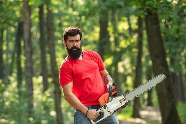 Ein gutaussehender junger Mann mit Bart trägt einen Baum. Der illegale Holzeinschlag dauert bis heute an. Holzfäller im Wald mit Motorsägenbeil. — Stockfoto
