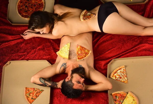 Pizza party. Couple relaxing in bed with pizza. Pizza delivery. Beautiful girl nude body and bearded macho. Snack after sex. Lazy couple spend time in bedroom. Sexy couple eat pizza in bed