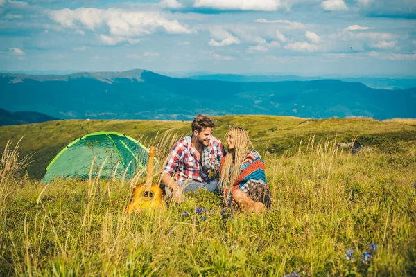 Enjoying the beautiful landscape of couples camping in the mountains. Happy couple tourists man and woman having a rest beside camp, guitar and sunny day.