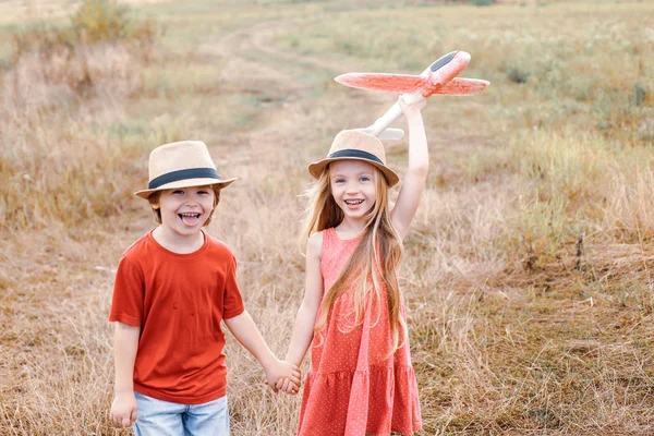 Crianças se divertindo com avião de brinquedo em campo contra o fundo da natureza. Menino feliz e menina bonito jogar no avião ao ar livre. Sonhos de aviões voadores . — Fotografia de Stock