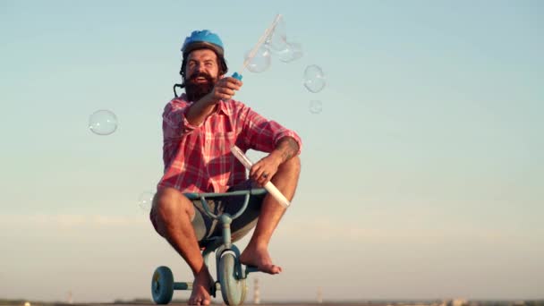 Ο τρελός αστείος άνθρωπος καβαλάει ένα ποδήλατο στο φόντο του ουρανού. Αστείος άνθρωπος με παιδικό ποδήλατο σε ένα εξοχικό δρόμο. Αστείος άνθρωπος κάνει αστεία πρόσωπα. — Αρχείο Βίντεο