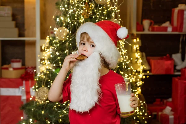 Happy Santa Claus - little child boy with glass of milk and cookie. Portrait of surprised and funny Santa. Cookies for kids Santa Claus. Santa Claus. Christmas child.