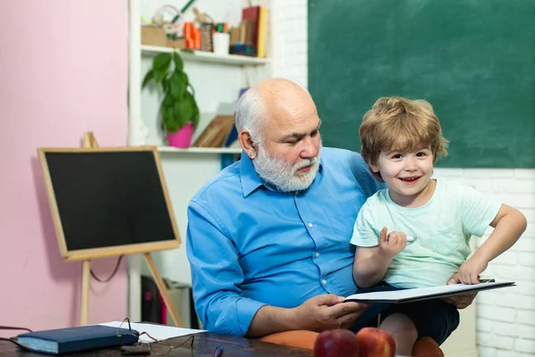 Junge aus der Grundschule auf dem Schulhof. Großvater und Enkel. freundlicher Junge mit alter, reifer Lehrerin im Klassenzimmer neben der Tafel. Familiengeneration und Beziehungskonzept. — Stockfoto