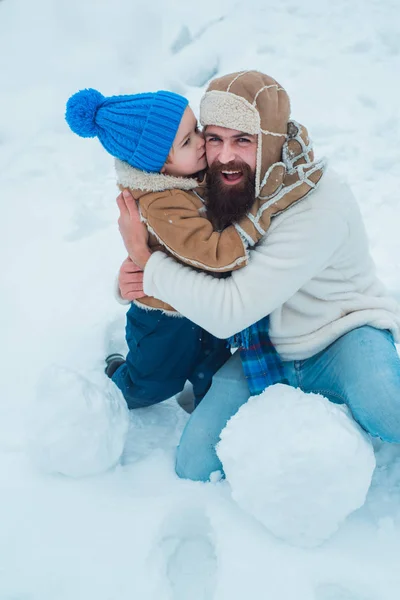 Папа і хлопчик посміхаються і обійматися. Син обіймає свого тата на зимовий відпочинок. Різдвяні свята і зима новий рік з батьком і сином. Батько і син грають з снігом в парку на білому снігу фону — стокове фото