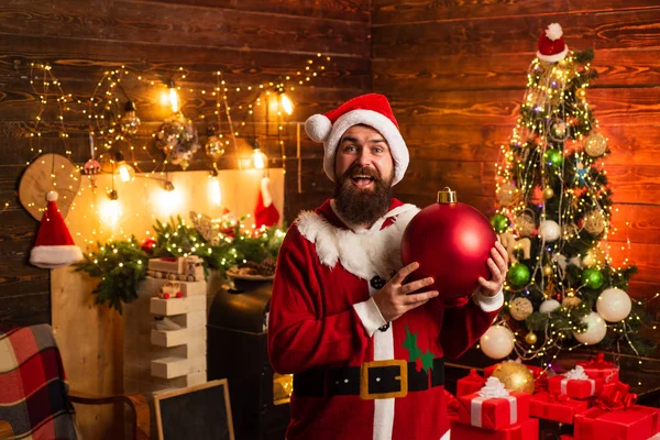 Hipster-Mann, bärtiger Weihnachtsmann feiern Erntedank und Weihnachten. Porträt des glücklichen Weihnachtsmannes mit dekorativen Spielzeugkugeln in der Nähe des Weihnachtsbaums. — Stockfoto