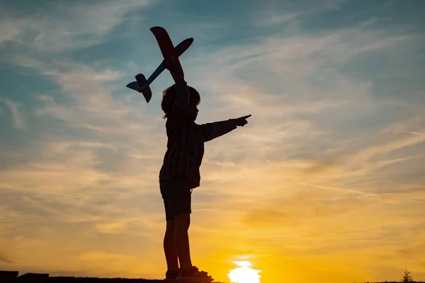 Child pilot with airplane dreams of traveling in summer in nature at sunset. Cute toddler boy playing outdoors. Child in the village with plane in his hands. Retro style airplane on sky background. — Stock Photo, Image