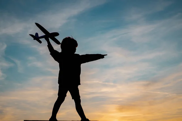 Silhouette of child with airplane in sunlight rays. Concept of dreams and travels. Dreams of flying planes. — Stock Photo, Image