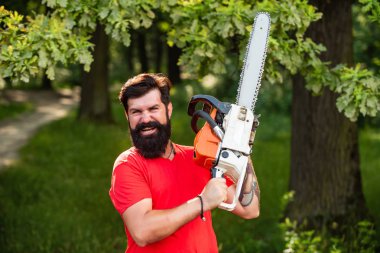 Orman arka plan üzerinde testere ile Lumberjack. Oduncu elektrikli testereyi tutuyor. Günlüğü. Ormanların yok olması, doğal ekosistemlerin toprak bozulması ve istikrarsızlaşmasının önemli bir nedenidir..