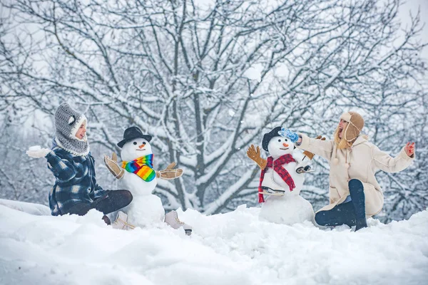 Hipster Girls przyjaciele gry z Snowman na śniegu Zima Krajobraz. Zimowe dziewczęta. Portret mody dwóch młodych modelek dziewczyna w pomieszczeniu z bałwana Bożego Narodzenia. — Zdjęcie stockowe