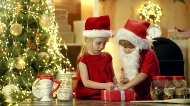 Noel Baba şapkalı iki mutlu sevimli çocuk noel var. Yeni yıl Noel konsepti. Mutlu çocuklar iki eliyle kırmızı bir hediye kutusu tutuyorlar. Noel Kutlaması tatili.