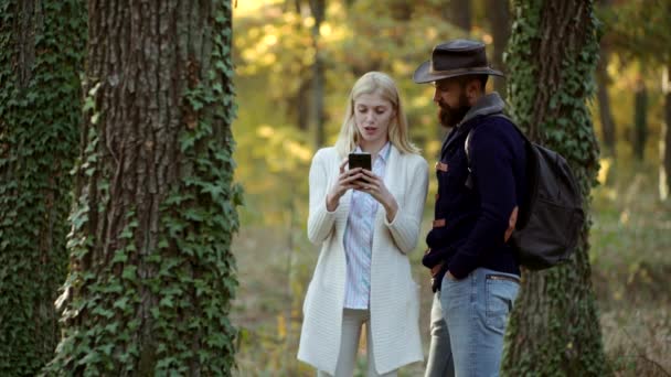Fashion portrait in autumn dress on nature background. Couple using smartphone outdoor. Cheerful carefree autumn couple in park on sunny day. Enjoying good weather. — Stock Video