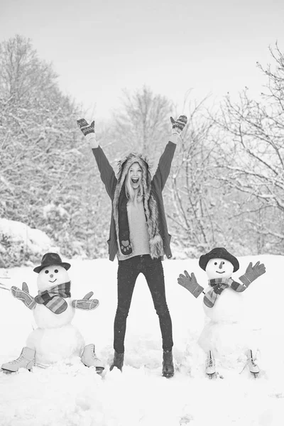 Funny snowman in stylish hat and scarf with funny girl on snowy field. Happy girl plaing with a snowman on a snowy winter walk. Happy girl snowman and winter fun. — Stock Photo, Image