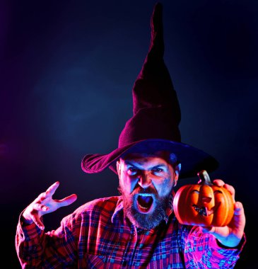 Karanlık arka planda korkunç yüzü olan cadılar bayramı adamı. Cadılar Bayramı, bayram kutlaması. Korkunç suratlı korkunç adam Balkabağı kafalı Jack Lantern 'i tutuyor.