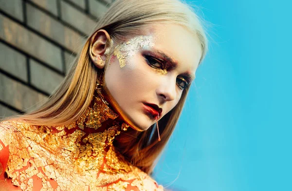 Mujer modelo de alta moda en brillantes destellos dorados. Belleza ojos dorados labios rojos sangrientos. Arte Cara de niña de piel dorada - retrato de cerca . — Foto de Stock