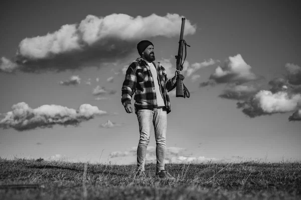 Vousatý muž lovec drží zbraň a procházky v lese. Hunter s brokovnicí zbraní na lov. — Stock fotografie
