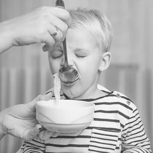 Mamma matar sonen. Pojke söt baby äter frukost. Barn äter soppa. Ungen söt pojke blå ögon sitta vid bordet med tallrik och mat. Hälsosam kost. Friska livsmedel. Ät hälsosamt. Småbarn som äter mellanmål hemma — Stockfoto