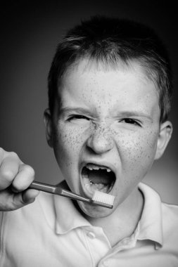 Çocuk temiz dişler diş fırçası ile. Gömlek tasarım, sağlık, ağız hijyeni. Diş fırçası izole kırmızı zemin üzerine el ile boy gülümseyerek. Mutlu küçük çocuk dişlerini fırçalıyor.