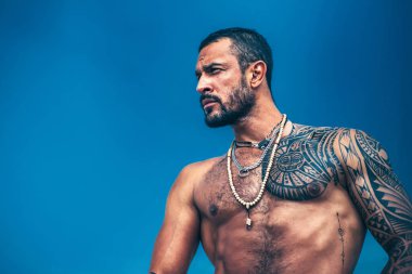 Kas latin aşığı. Kas vücut ile Latin adam ciddi görünüyor. Mavi gökyüzü arka plan üzerinde yakışıklı acımasız adam. Acımasız yakışıklı erkek model portresi.