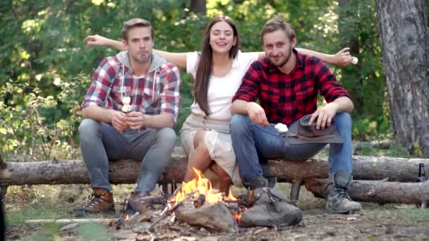 Ungdomar äter rostade marshmallows när de campar nära lägerelden. Vänners campingkoncept. Ungdomar som roar sig utomhus. — Stockvideo