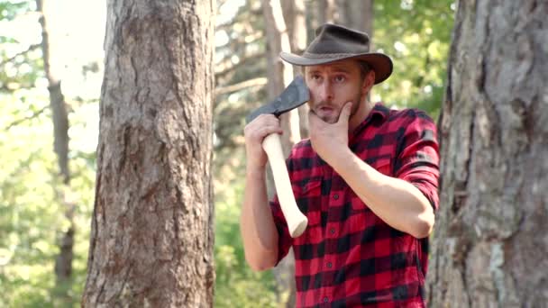 Snygg ung man med yxa nära skogen. Träskärare med yxa i sommarskogen. Skogshuggaren håller yxan. Skogshuggare stående med yxa på skog bakgrund. — Stockvideo