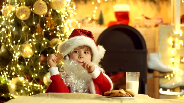 Маленький Санта собирает печенье и стакан молока дома. Санта - забавный ребенок, выбирающий кулинарию. Ребенок Санта-мальчика ест кулинарные блюда и пьет молоко . — стоковое видео