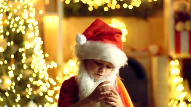 Babbo Natale bambino in possesso di biscotti di Natale e latte sullo sfondo dell'albero di Natale. Biscotti di Natale e latte. Giorno del Ringraziamento e Natale — Video Stock