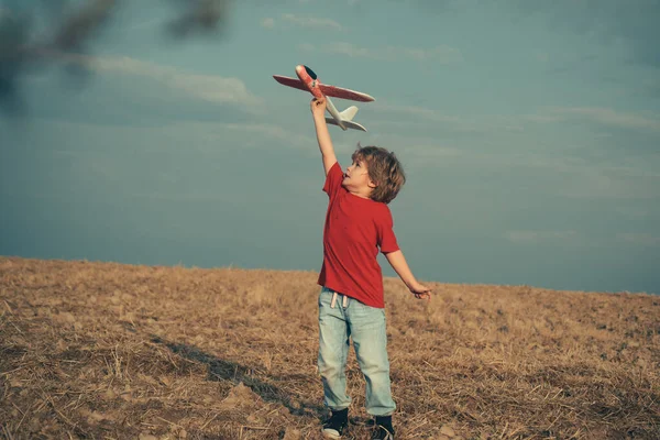 屋外の飛行機で幸せな少年の遊び。夢と旅の概念。飛行機の夢。青空を背景に野外でおもちゃの飛行機で楽しんでいる子供たち. — ストック写真