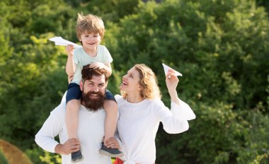 Mutlu bir aile. Anne ve baba, yaz aylarında doğada oyuncak kağıt uçakla çayırda. Baba, anne ve oğul birlikte oynuyorlar. Çocuk Bakımı.