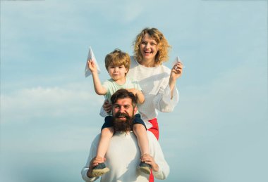 Aile tatili ve birliktelik. Bahar zamanı. Mutlu çocuk ailesine kağıt uçak gösteriyor. Mutlu baba portresi oğlu omuzlarında piggyback binmek veren ve yukarı bakıyor.