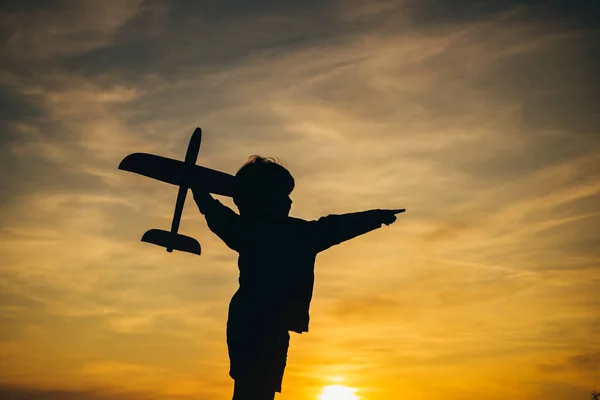 Silueta negra de lindo niño feliz corriendo por el campo y sosteniendo el avión de juguete en la mano. Niño feliz en el campo de verano. Niño pequeño está jugando y soñando con volar sobre las nubes . — Foto de Stock