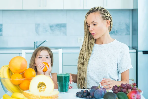 Mulher feliz mãe e menina filha bebe smoothie verde na cozinha. Feliz família amorosa mãe e filha segurar xícara de smoothie verde fresco. Vegan dieta refeição em casa. Comer crianças . — Fotografia de Stock