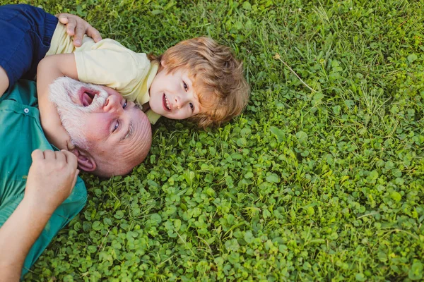 Büyükbaba ve torunun yeşil çimlerde kucaklaşıp kucaklaşsın. Büyükbaba, Oğul ve Torunuyla Park 'ta eğleniyor. Erkek nesli. Aile yazı ve aktif tatiller.