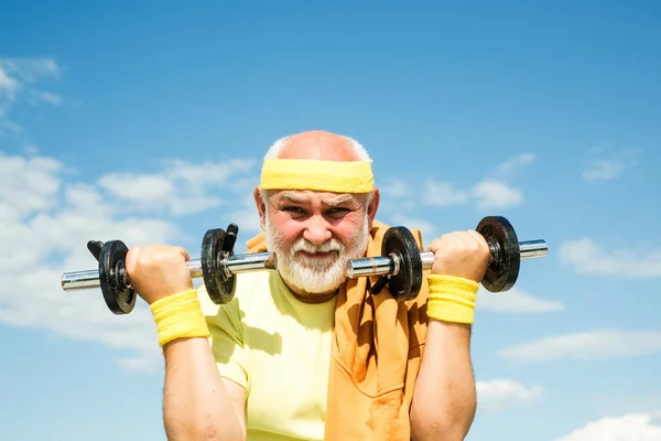 Happy Senior man oefenen met heffen halter outdoor. Grootvader sporter portret op blauwe lucht achtergronden. Senior sportman in sportcentrum. — Stockfoto