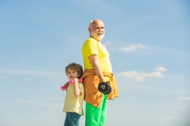 Her gün egzersiz yapıyoruz. Ellerinde dambıllar olan büyükbaba ve torun. Çocuklar büyükbabalarından sonra egzersizleri tekrarlıyorlar. Dambılı atletik aile.